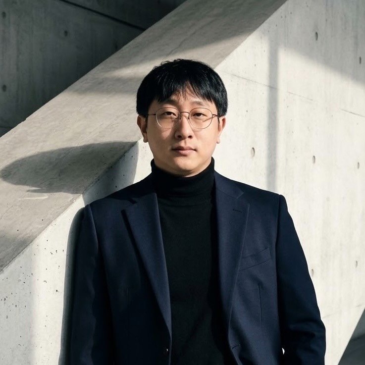 Portrait of Philly in a black turtleneck and blazer against a concrete wall
