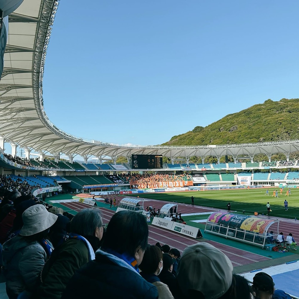 Transcosmos Stadium Nagasaki seen from the stands, with green hills behind the roof